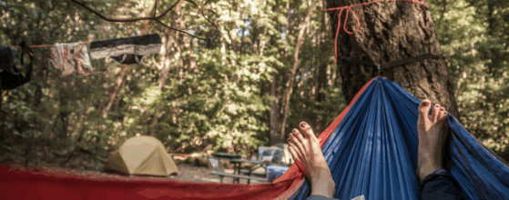 Abbildung einer Person die in einer Hängematte beim Camping liegt